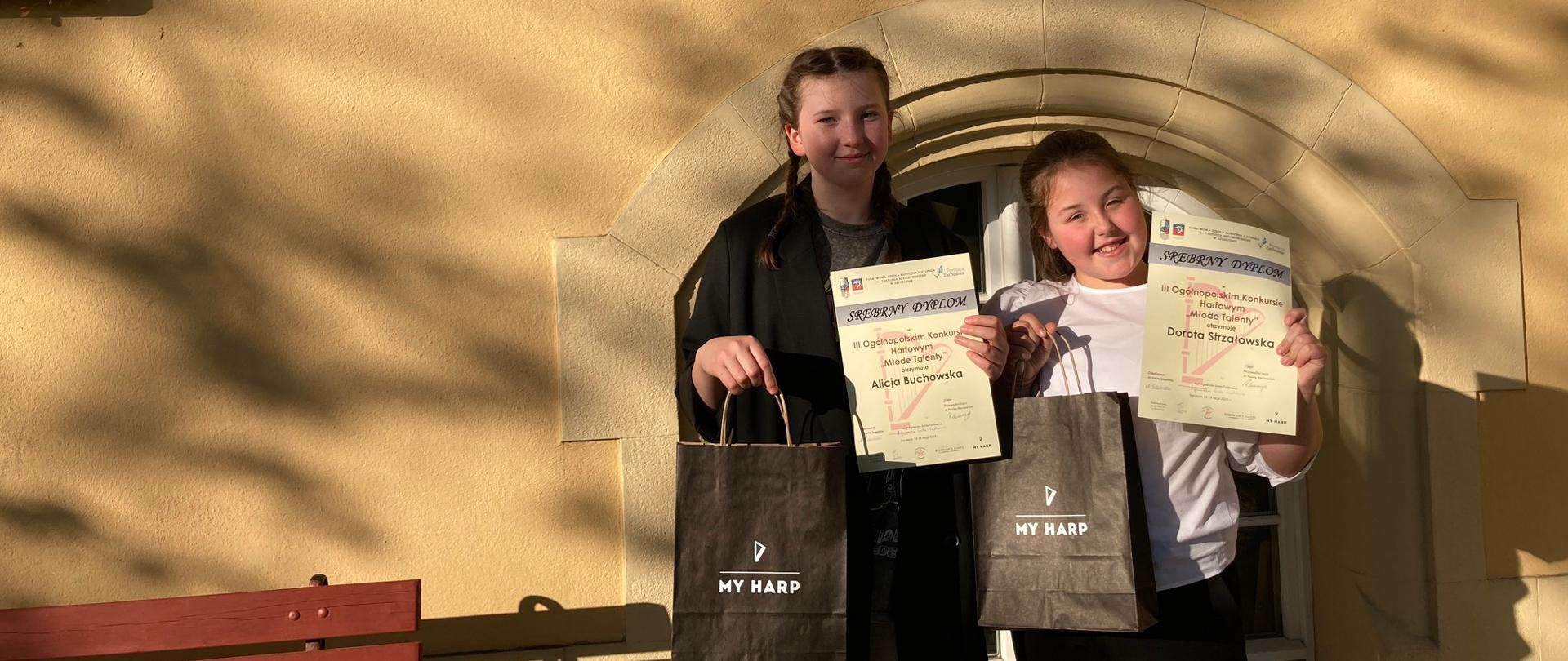 Uczennice z dyplomami i nagrodami przed budynkiem szkoły w Szczecinie.