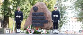 Żołnierze Marynarki Wojennej stoją po dwóch stronach pomnika przed którym leżą wiązanki.