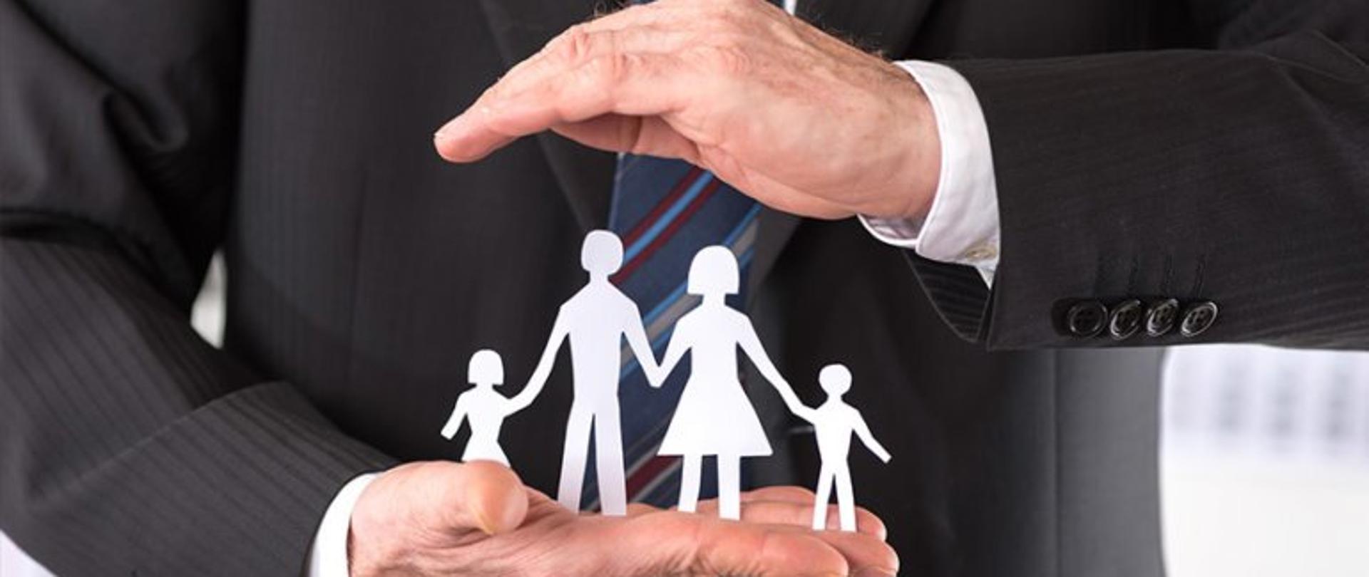 Fragment męskiego korpusu z widocznymi dłońmi, które zamykają postacie rodziny wycięte z papieru