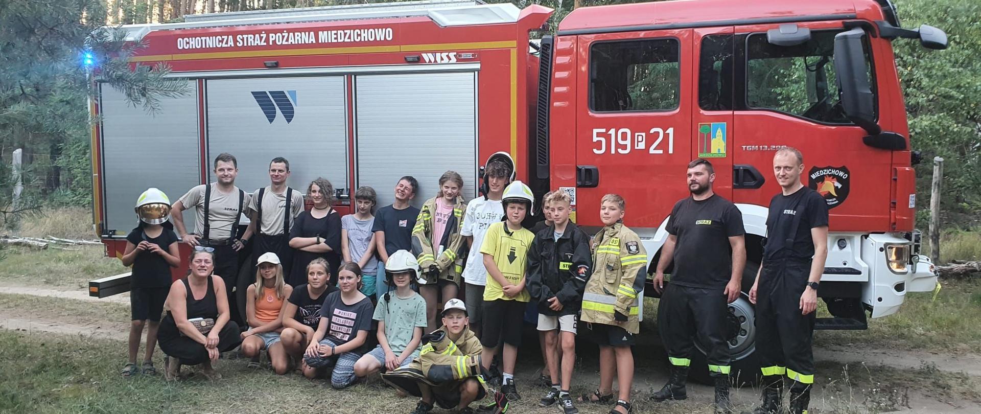 Zdjęcie grupowe dzieci wraz ze strażakami na tle wozu bojowego.