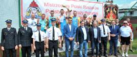 Na zdjęciu znajdują się strażacy którzy brali udział w mistrzostwach oraz osoby cywilne. Stoją na tle baneru z napisem : Mistrzostwa Polski Strażaków PSP w Siatkówce Plażowej