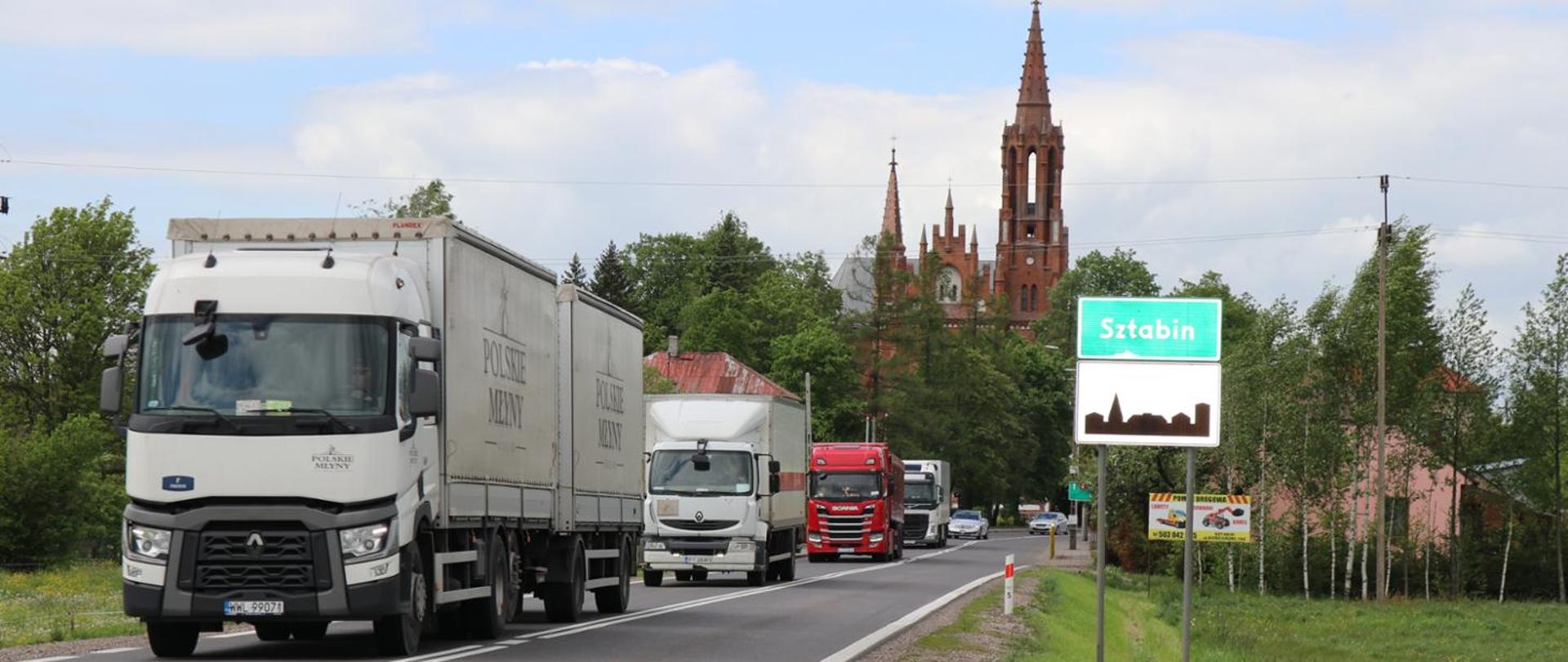 DK8 Sztabin samochody ciężarowe na wąskiej drodze, na drugim planie zabudowania i kościół