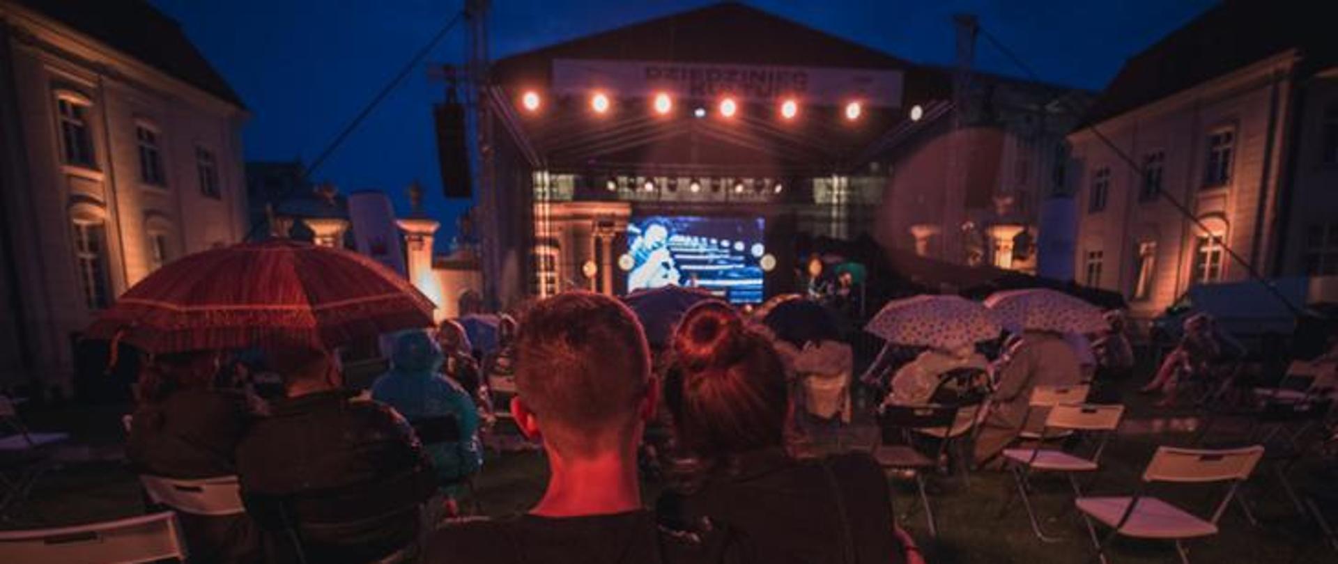 Ludzie siedzący w plenerze, oglądający film.