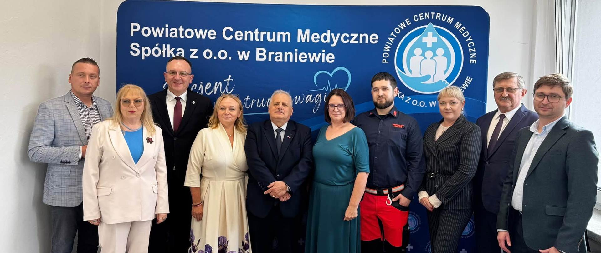 Grupa ludzi stoi na tle niebieskiej ścianki 