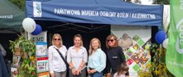 Grupa czterech kobiet i dziewczynka w tiulowej spódniczce stoją przed granatowym namiotem handlowym Państwowej Inspekcji Ochrony Roślin i Nasiennictwa 