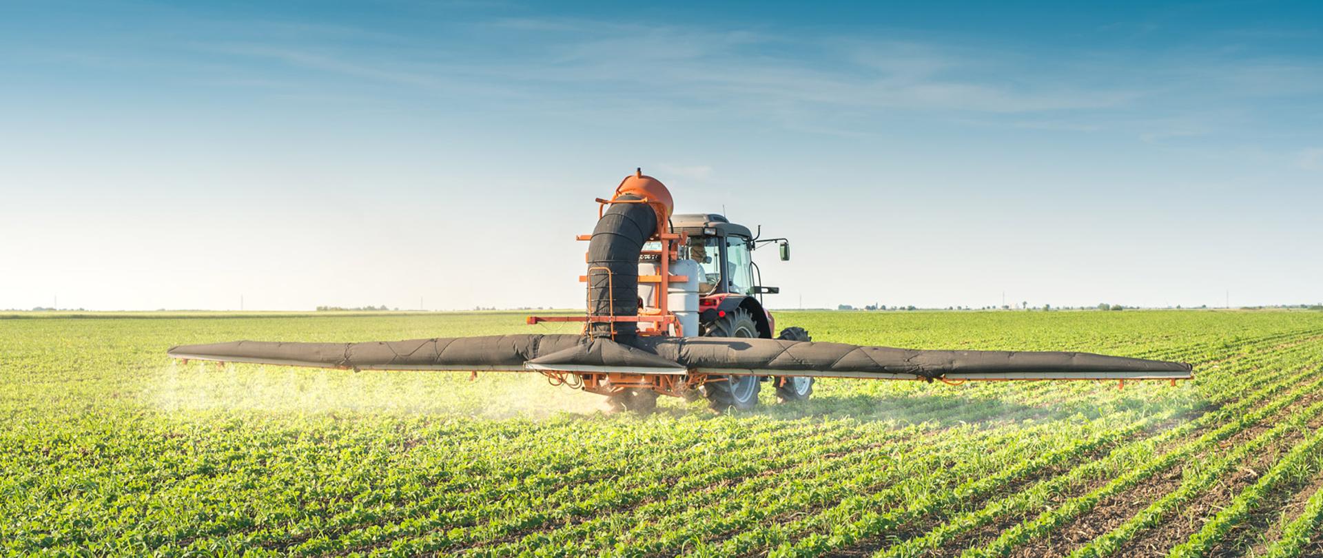Ciągnik rolniczy rozpyla środki ochrony roślin nad uprawami