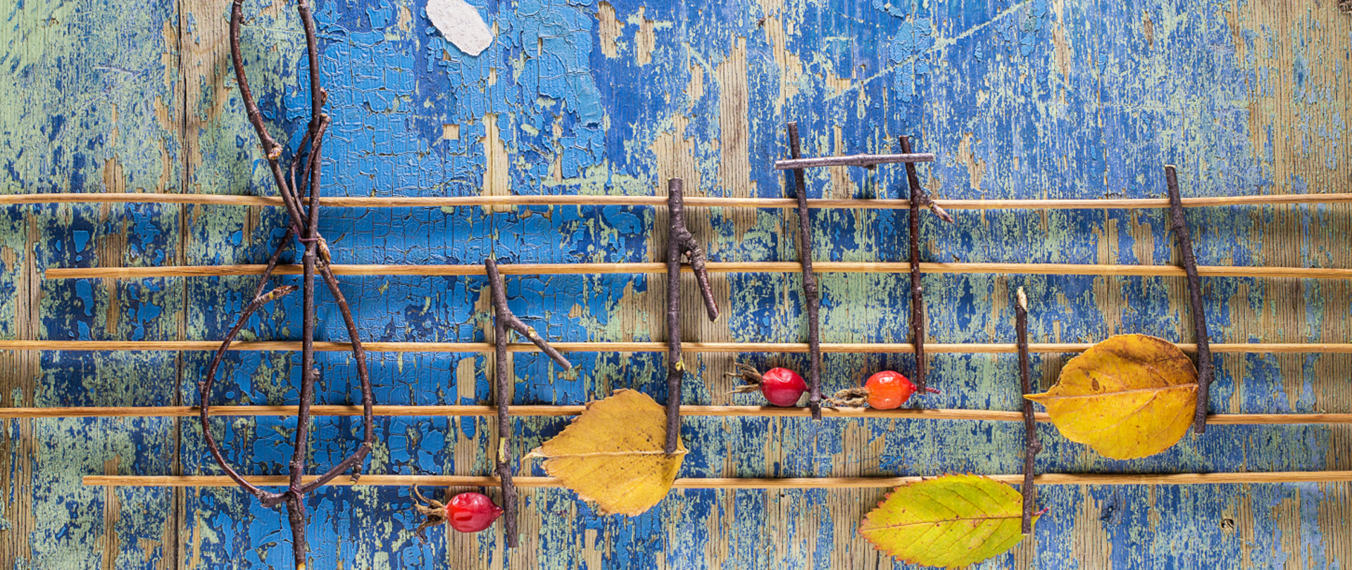 Obraz przedstawia pięciolinię złożoną z liści, owoców i gałęzi, na niebieskim, drewnianym tle.