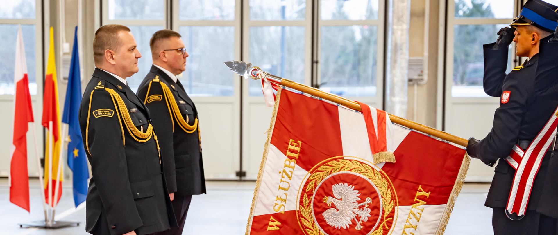 komendant miejski PSP w Łodzi oraz zastępca komendanta miejskiego PSP w Łodzi przejmujący obowiązku służbowe stoją przed sztandarem na czerwonym dywanie