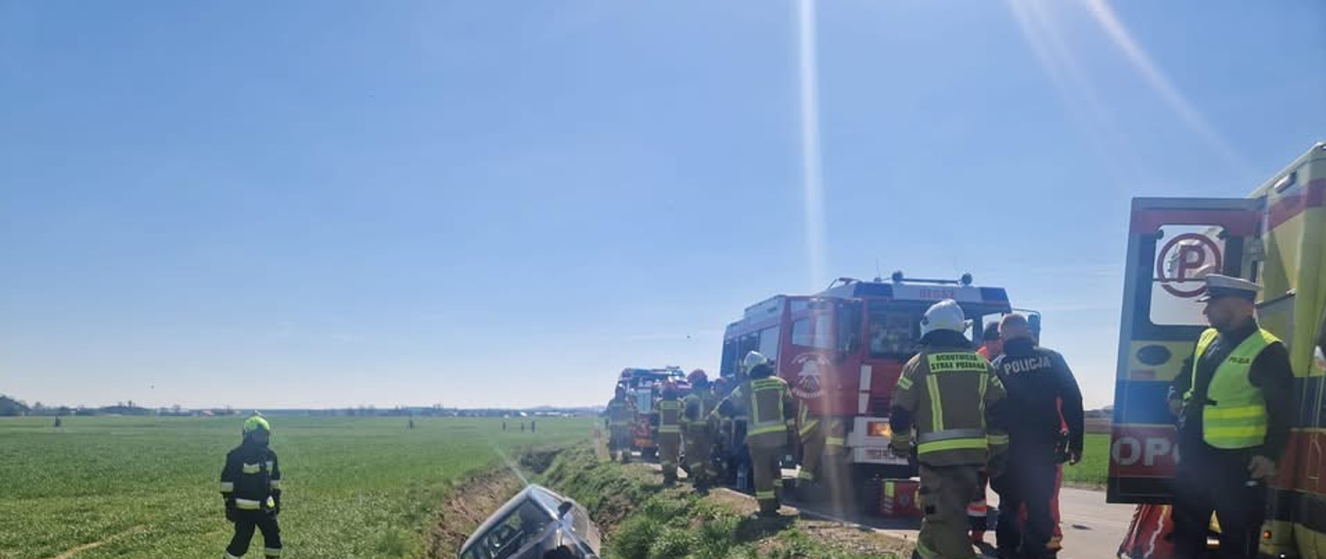 Na zdjęciu widać samochód w rowie oraz samochody pożarnicze
