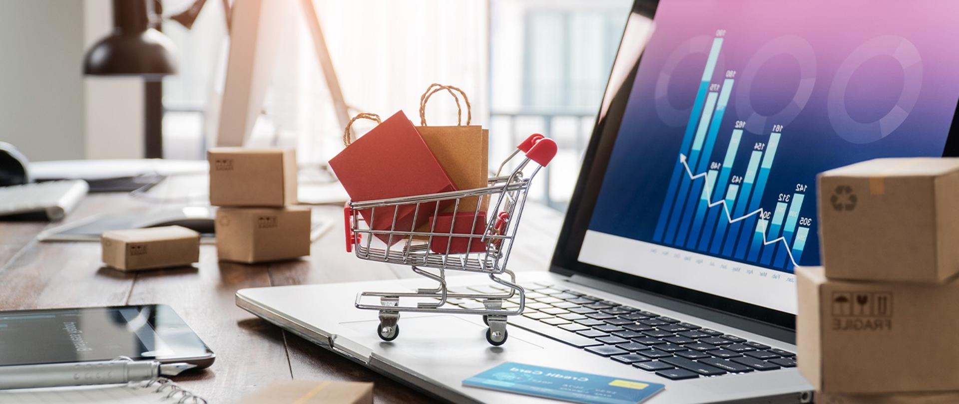 Zaproszenie na debatę "Rynek Przyszłości. Dokąd zmierza e-commerce?", która odbędzie się 28 kwietnia br. o godz. 10:00. Na zdjęciu widać biuro, a na nim laptop, karta, małe paczuszki i mały koszyk, w którym są torby papierowe.