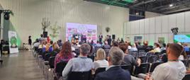 Publiczność siedzi na sali podczas konferencji branżowej, na scenie odbywa się prezentacja z udziałem prelegentów; w tle widoczny napis „KONKURS ROŚLIN NOWOŚCI 2023”.