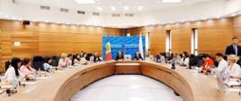 Nowoczesna sala konferencyjna. Przy dużym drewnianym zaokrąglonym stole siedzi kilkanaście osób, uczestników szkolenia. W tle widoczne są flagi Mołdawii, Unii Europejskiej i Polski.