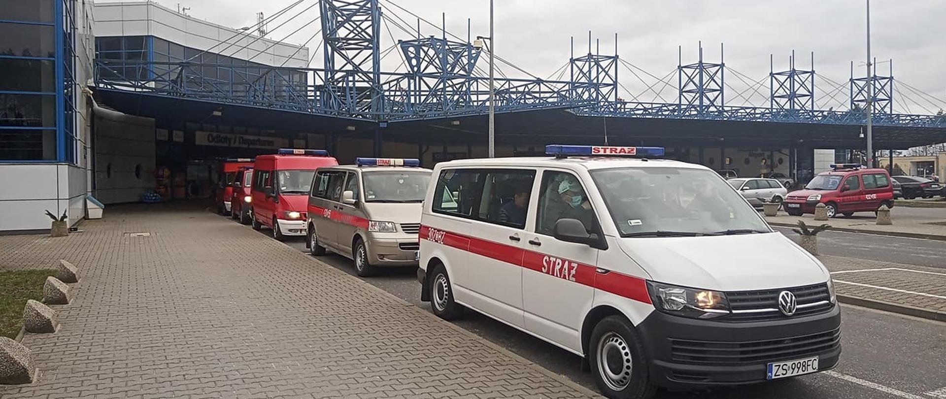 Busy Państwowej Straży Pożarnej ustawione na lotinsku Goleniów w celu transportu obywateli Ukrainy do punktu recepcyjnego. Widoczne 6 samochodów, w tle lotnisko goleniów.