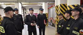 Na zdjęciu widać funkcjonariuszy PSP w umundurowaniu koszarowym, specjalnym oraz wyjściowym. Zdjęcie w pomieszczeniach komendy. Oświetlenie sztuczne. Podłoże z płytek.