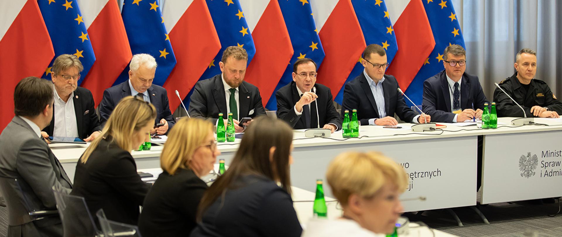 Na zdjęciu widać siedzących za stołem w trakcie wideokonferencji z wojewodami m.in. ministra Mariusza Kamińskiego, ministra Łukasza Szumowskiego, wiceminister Maciej Wąsik, wiceminister Paweł Szefernaker, Szef GIS Jarosław Pinkas , wiceminister zdrowia Waldemar Kraska i komendant główny PSP st. bryg. Andrzej Bartkowiak.