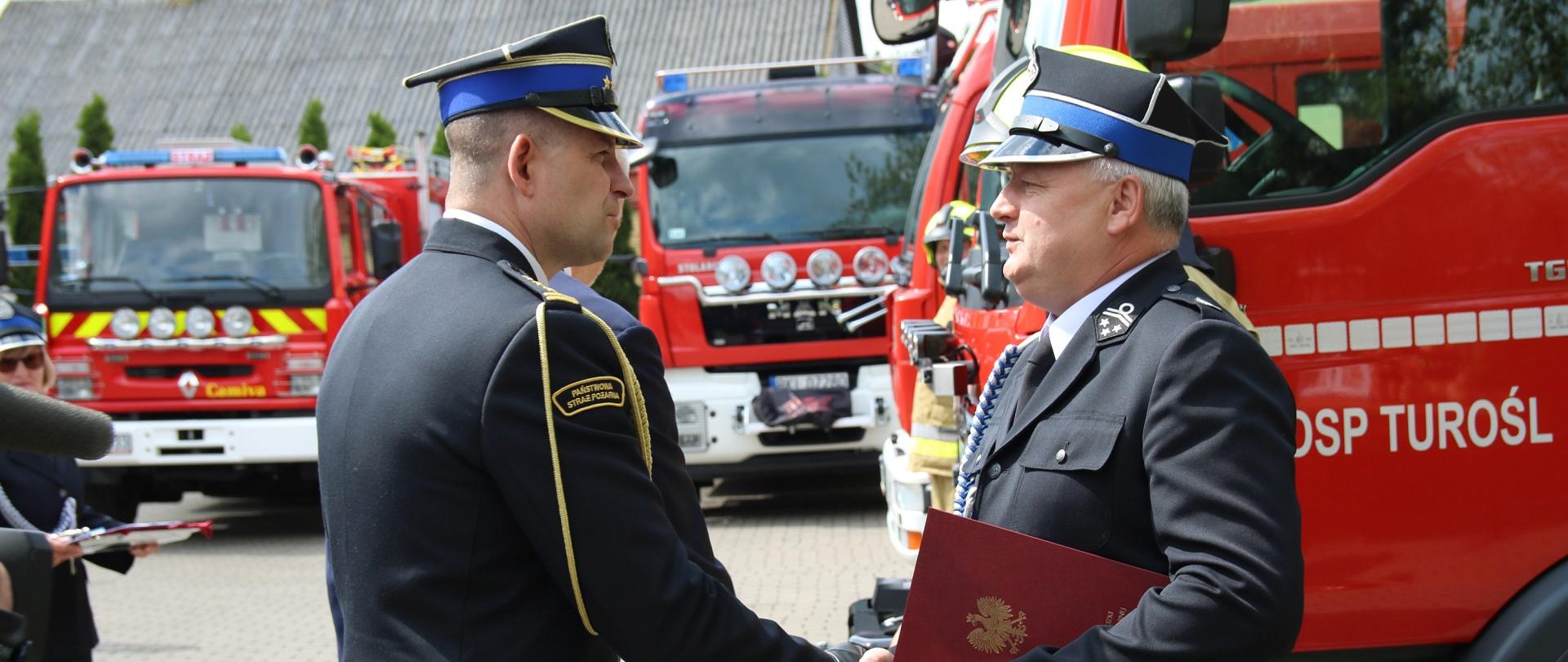 Na pierwszym planie Podlaski Komendant Wojewódzki i druh OSP, w tle pojazdy pożarnicze.
