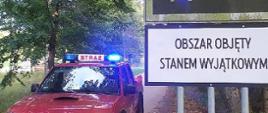 Montaż tablic informacyjnych na terenie obszaru objętego stanem wyjątkowym, widoczna tablica miejscowości i pojazd strażacki.