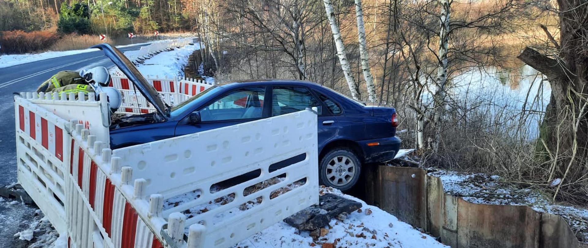 Zdjęcie przedstawia auto które wypadło podczas wypadku z pasa drogi. w tle widać jezioro.