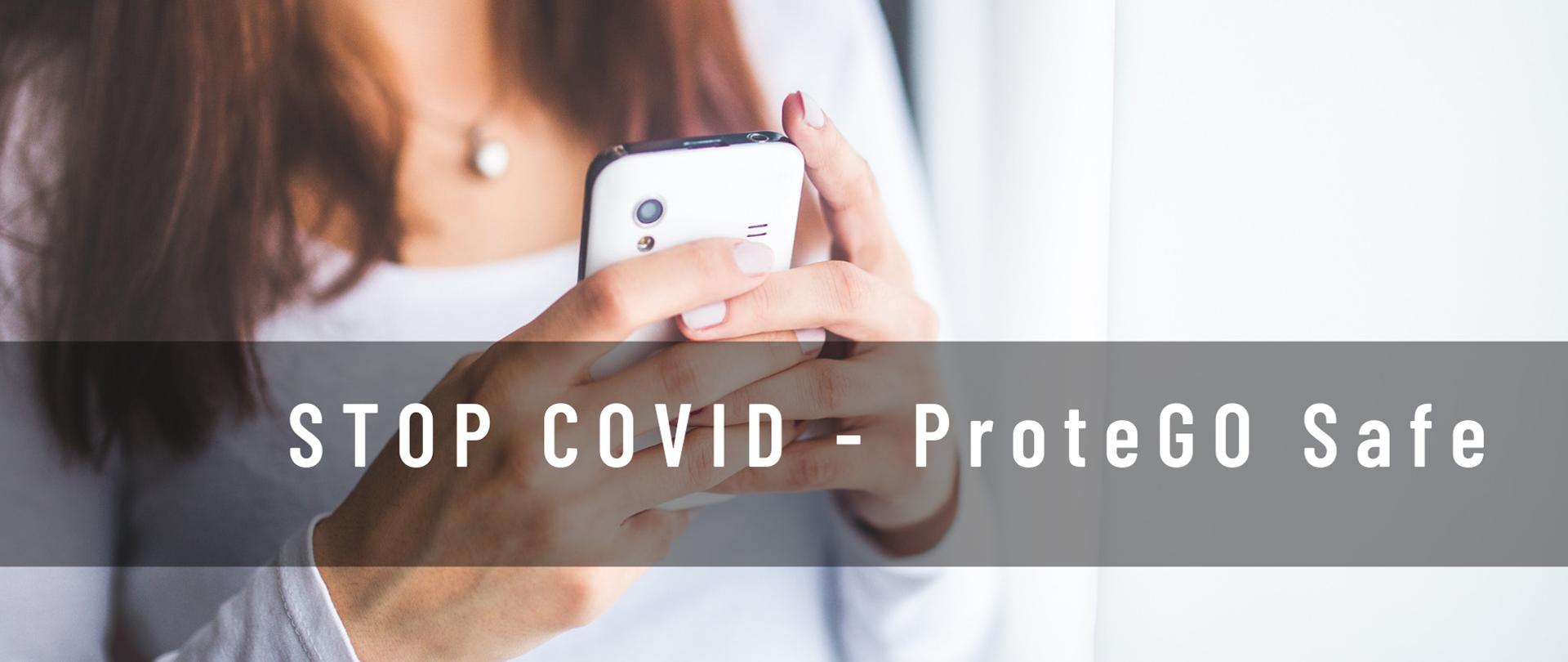 Zdjęcie to baner reklamowy STOP COVID ProteGO Safe przedstawiający kobietę trzymającą smartfon