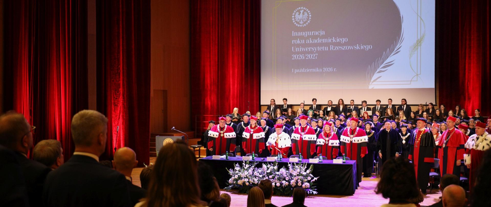 Władze uczelni i zaproszeni goście stoją. na ekranie slajd z napisem: Inauguracja roku akademickiego Uniwersytetu Rzeszowskiego 2026/2027 1 października 2026 r.