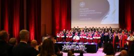 Władze uczelni i zaproszeni goście stoją. na ekranie slajd z napisem: Inauguracja roku akademickiego Uniwersytetu Rzeszowskiego 2026/2027 1 października 2026 r.