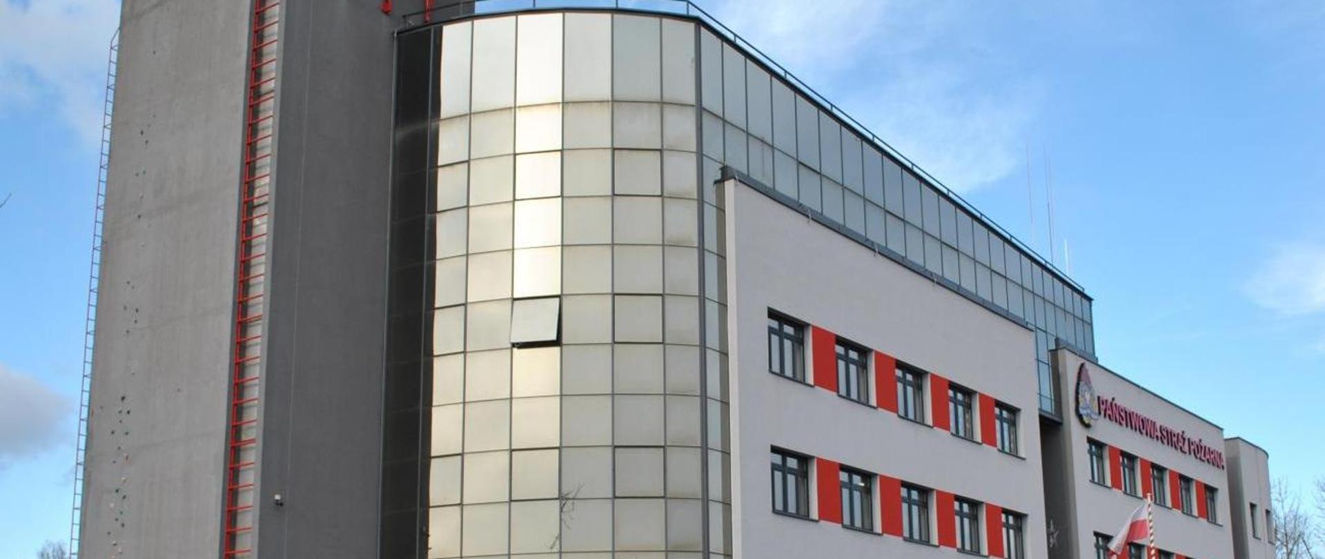 Zdjęcie budynku Komendy Wojewódzkiej PSP w Krakowie. Z prawej strony zdjęcia widać dwa rzędy okien z czerwonymi wstawkami. Nad nimi widnieje napis Państwowa Straż Pożarna. Z lewej strony budynku znajduje się czerwona drabina.