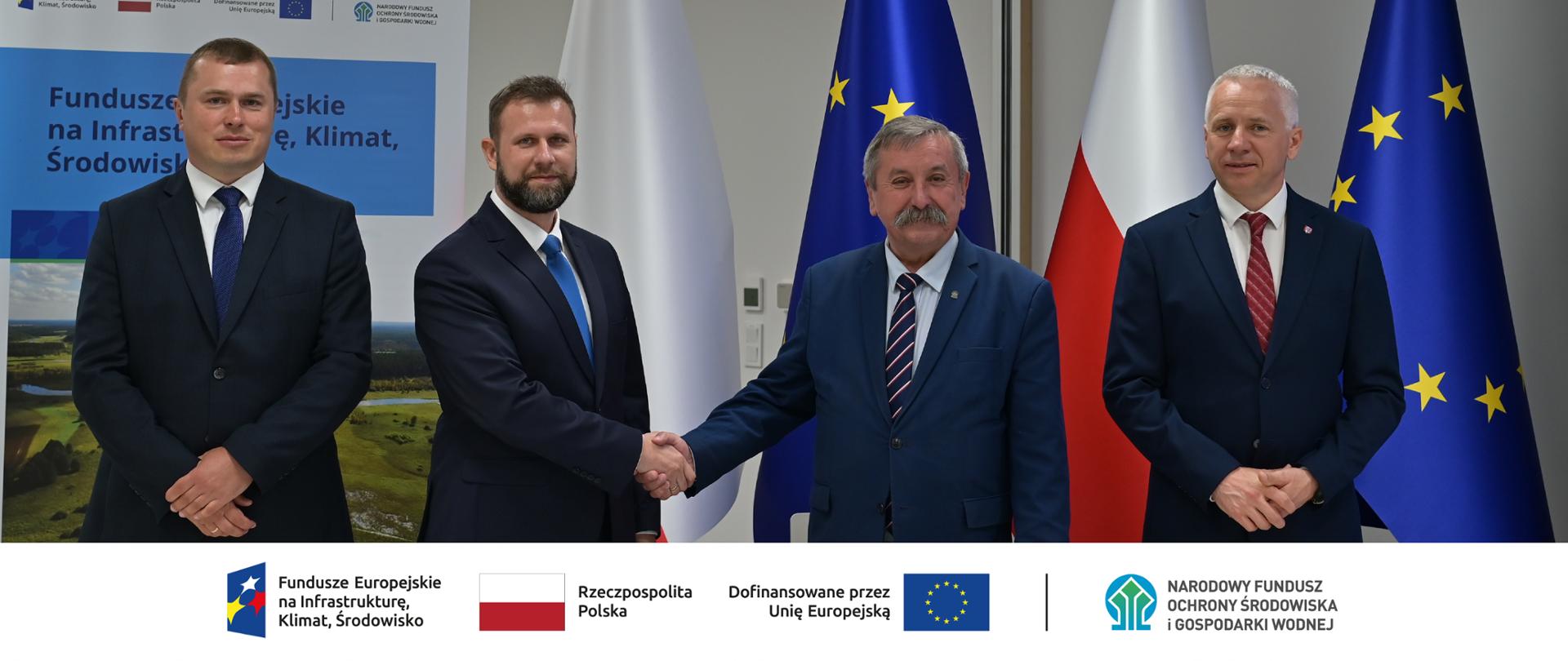 Zdjęcie grupowe. Czterej mężczyźni podczas uroczystego podpisania umowy. W stopce grafiki ciąg logotypów: Fundusze Europejskie na Infrastrukturę, Klimat, Środowisko, flaga Rzeczypospolita Polska, flaga UE i Dofinansowane przez UE, NFOŚiGW.