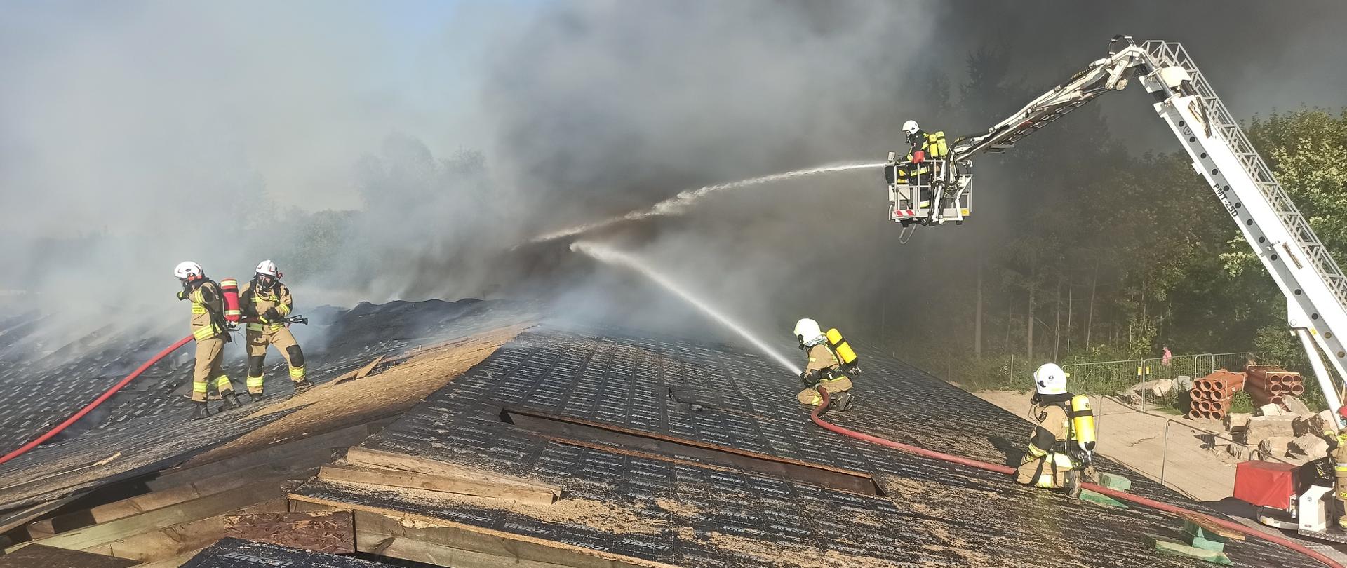 Na zdjęciu strażacy ubrani w ubrania ochronne i aparaty ochrony dróg oddechowych gaszący pożar szpitala z dachu.