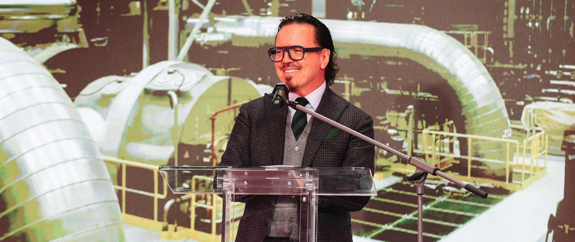 Minister Wojciech Balczun stoi za mównicą. W tle ekran z prezentacją.