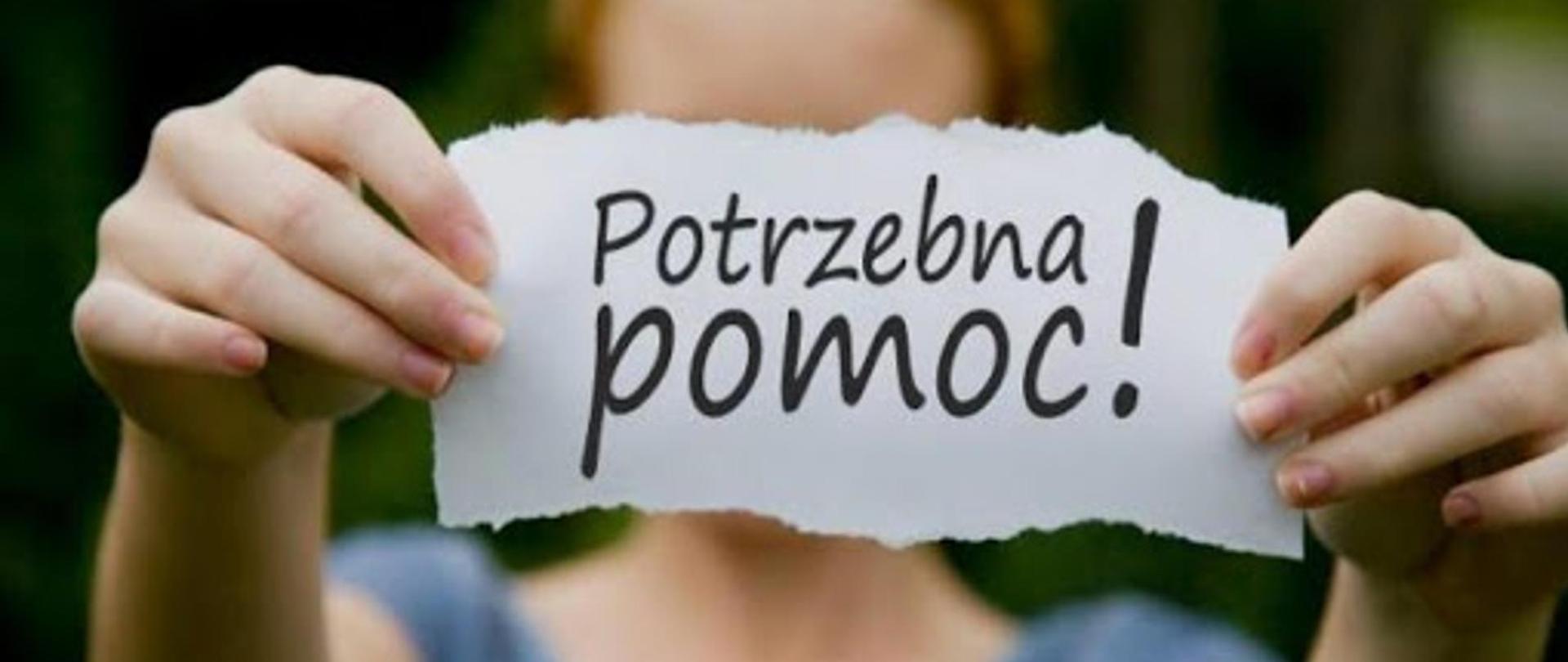 Potrzebna pomoc. Apel o pomoc. Na grafice osoba trzymająca oburącz kartkę z napisem "Potrzebna pomoc!". Tło rozmyte.