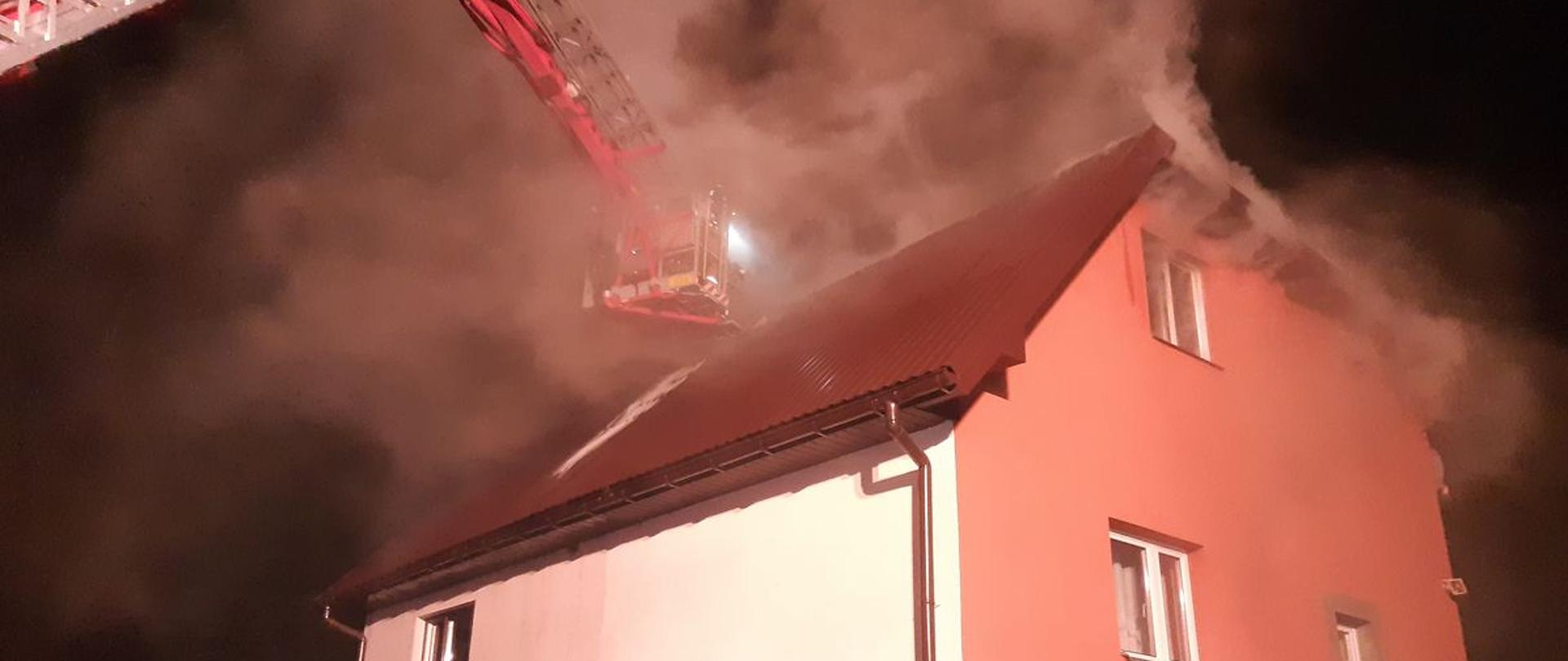 Strażacy prowadzą działania z podnośnika przy budynku z którego unosi się dym