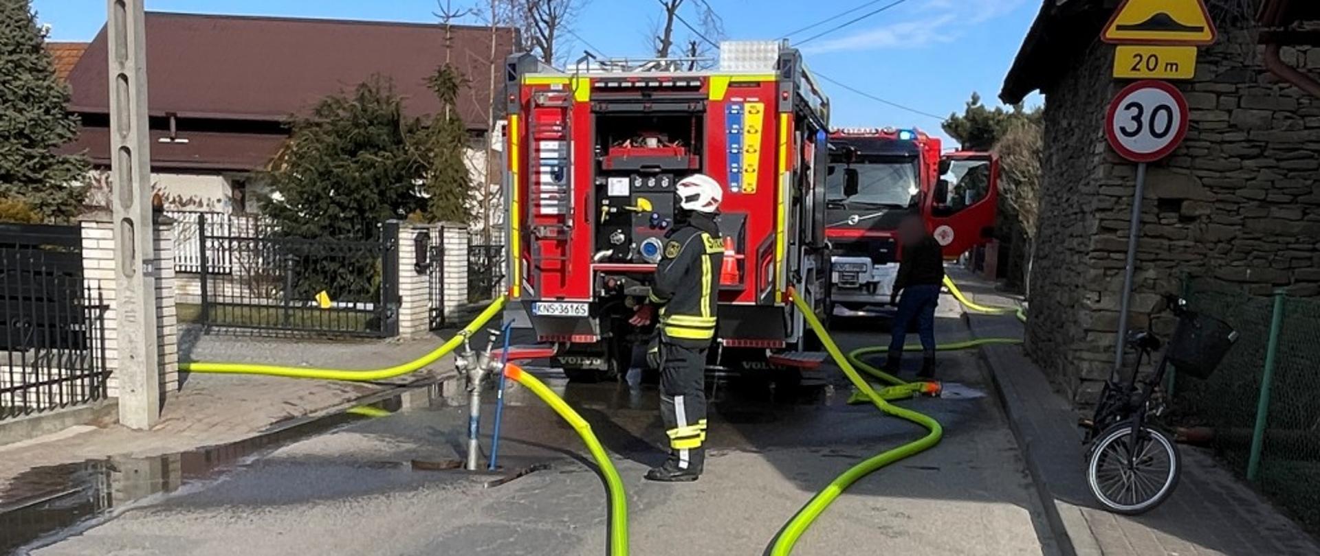 Kierowca ratownik obsługuje autopompę, woda jest dostarczana żółtymi wężami do pożaru 