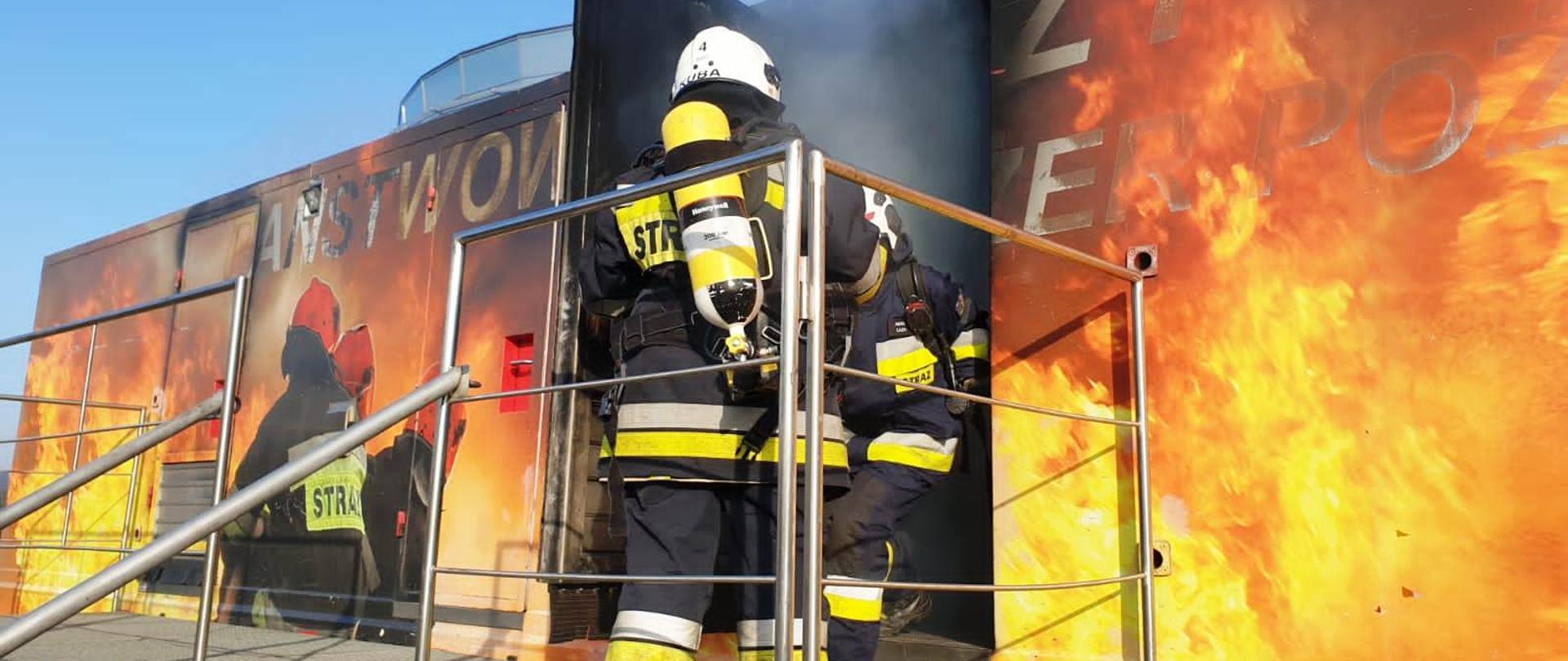 Komora ogniowo rozgorzeniowa na niej namalowanie płomienie oraz trzech strażaków. Z otwartych drzwi komory wydobywa się dym i dwóch strażaków jeden wychodzi a drugi stoi tyłem.