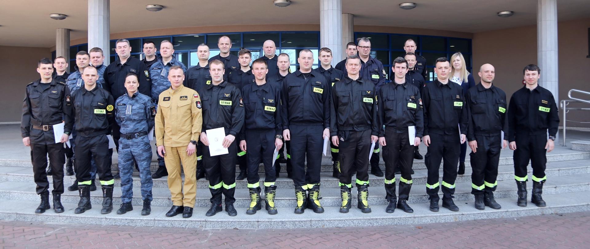 Grupowe zdjęcie uczestników szkolenia w towarzystwie Zastępcy Komendanta Centralnej Szkoły PSP oraz pracowników Szkoły sprawującymi nadzór nad szkoleniem