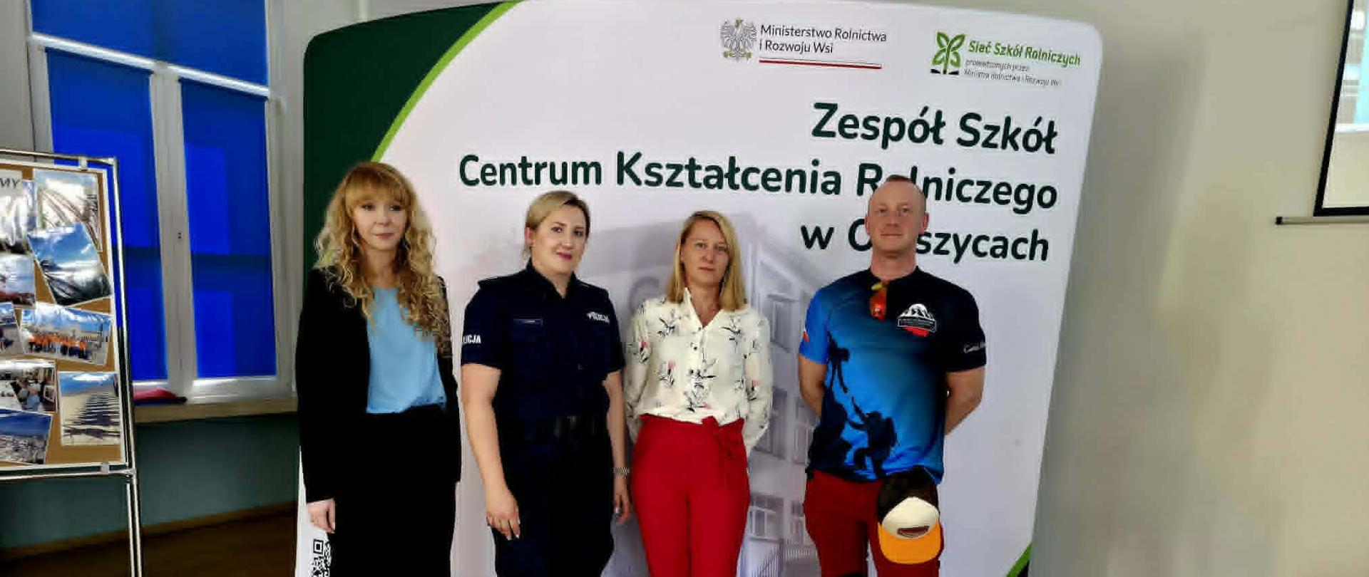 Cztery osoby pozują do wspólnego zdjęcia przed ścianką promującą Zespół Szkół Centrum Kształcenia Rolniczego w Oleszycach po zakończeniu spotkania profilaktycznego.