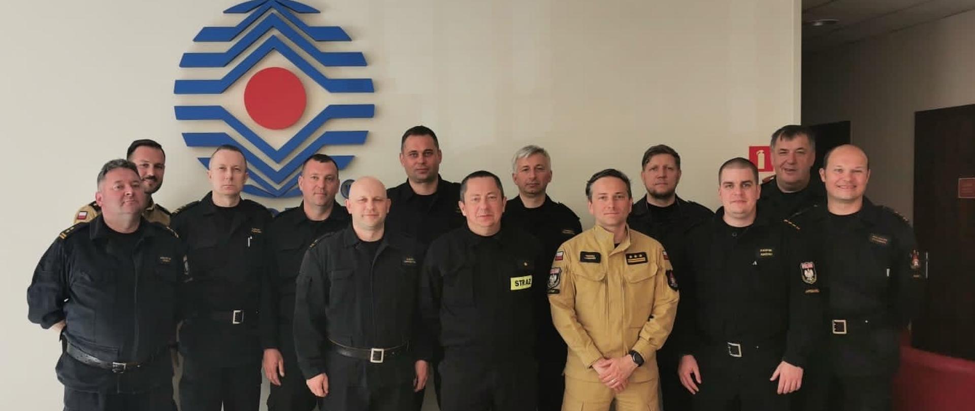 Zdjęcie grupowe uczestników spotkania. Na zdjęciu 13 stojących oficerów w tle logo CNBOP. 
