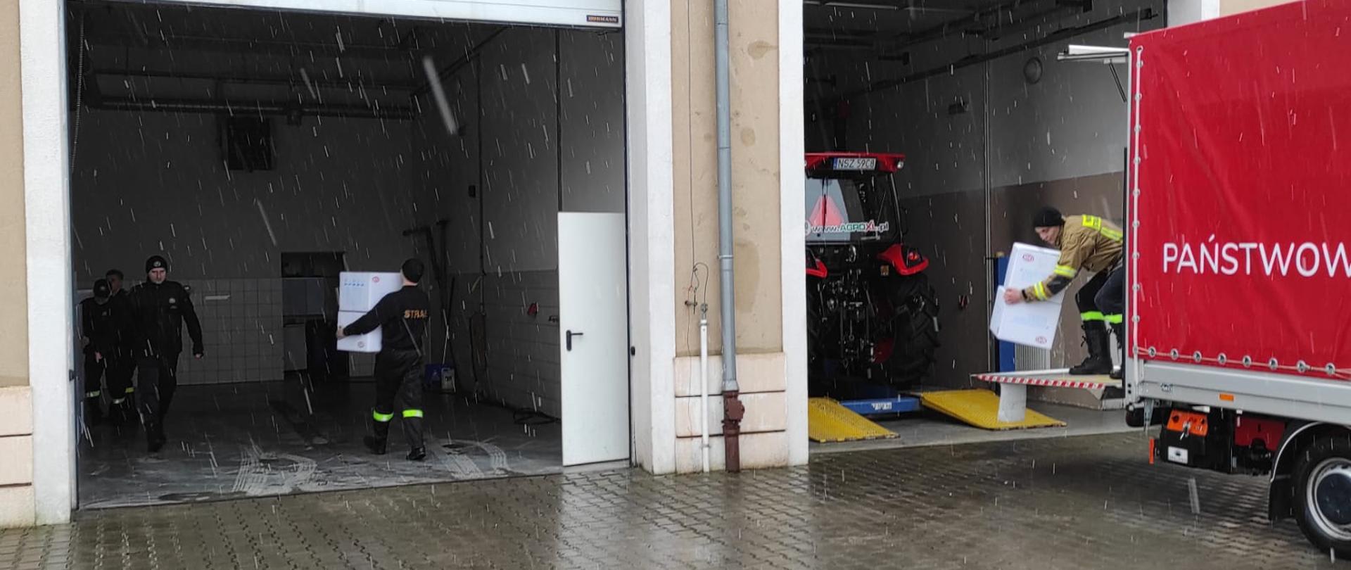 Zdjęcie przedstawia strażaków rozpadujących transport z maseczkami ochronnymi dla ludności powiatu szczycieńskiego