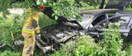 Zdjęcie przedstawia uszkodzony pojazd osobowy w obrębie, którego strażacy prowadzą działania