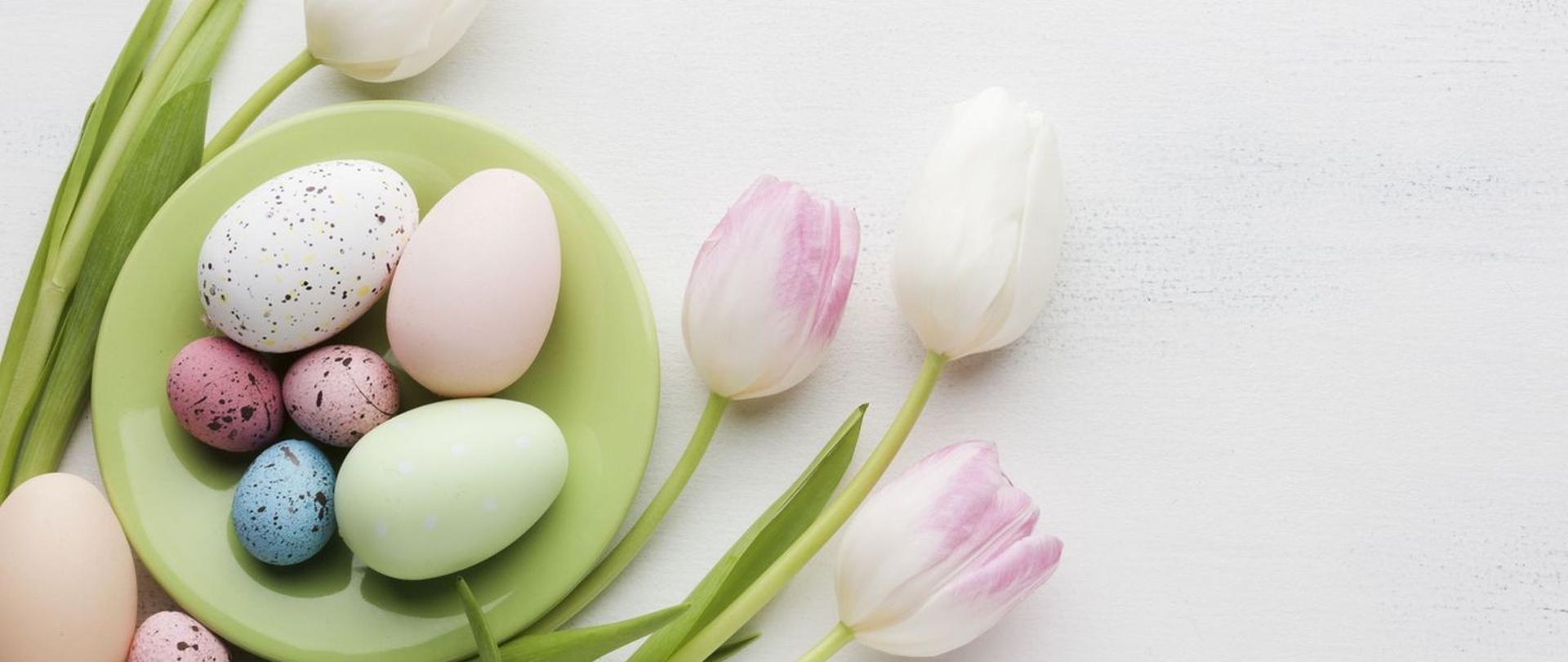 obraz przedstawia dekorację świąteczną (wielkanocną . Na dole po prawej na zielonym talerzu ułożone kolorowe jajka wokół dekoracja z tulipanów.