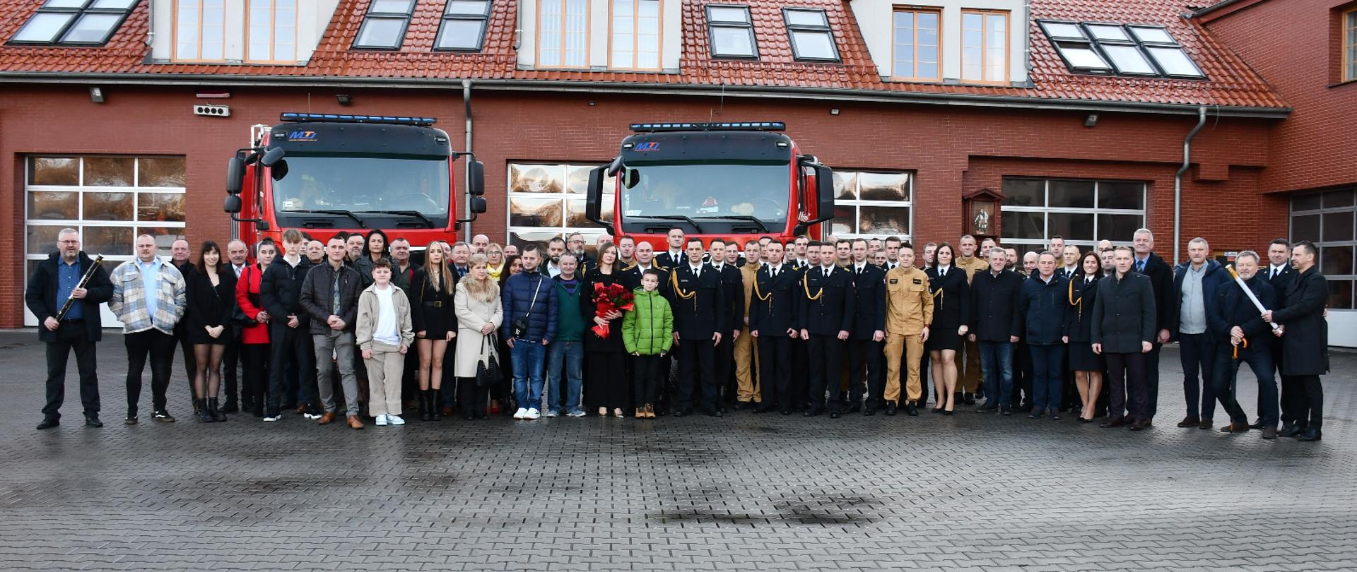 Zdjęcie grupowe strażaków i zaproszonych gości na tle pojazdów pożarniczych.