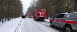 Na zdjęciu na ośnieżonej drodze przy prawej krawędzi stoją samochody strażackie 