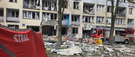 Teren gruzowiska i budynek po wybuchu gazu, samochód straży pożarnej stoi przed budynkiem
