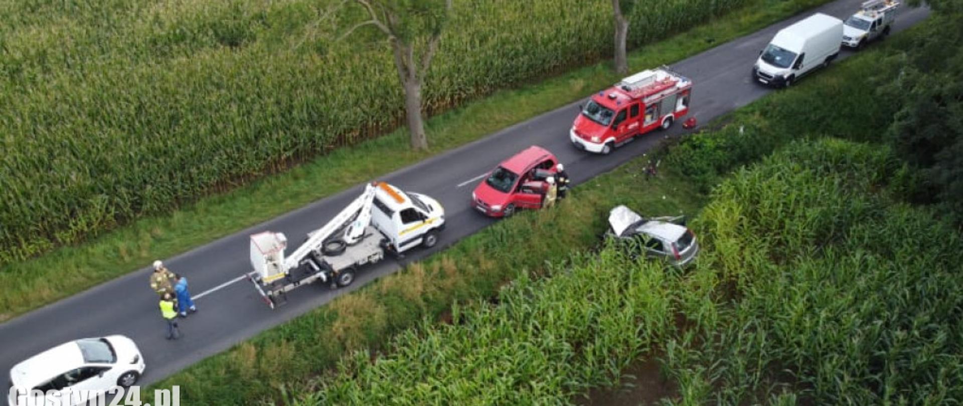 Zdjęcie z lotu ptaka, przedstawia samochody osobowe stojące na drodze oraz samochód, który uderzył w drzewo i leży na poboczu.