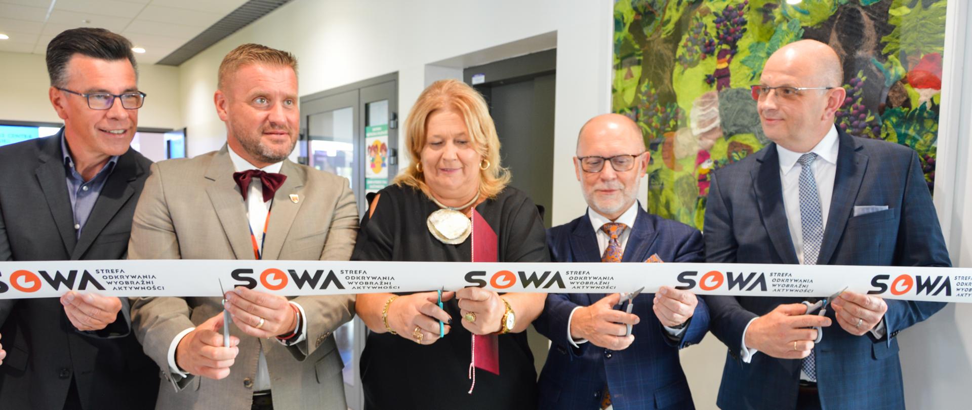 Kobieta i czterech mężczyzn przecinają wstęgę