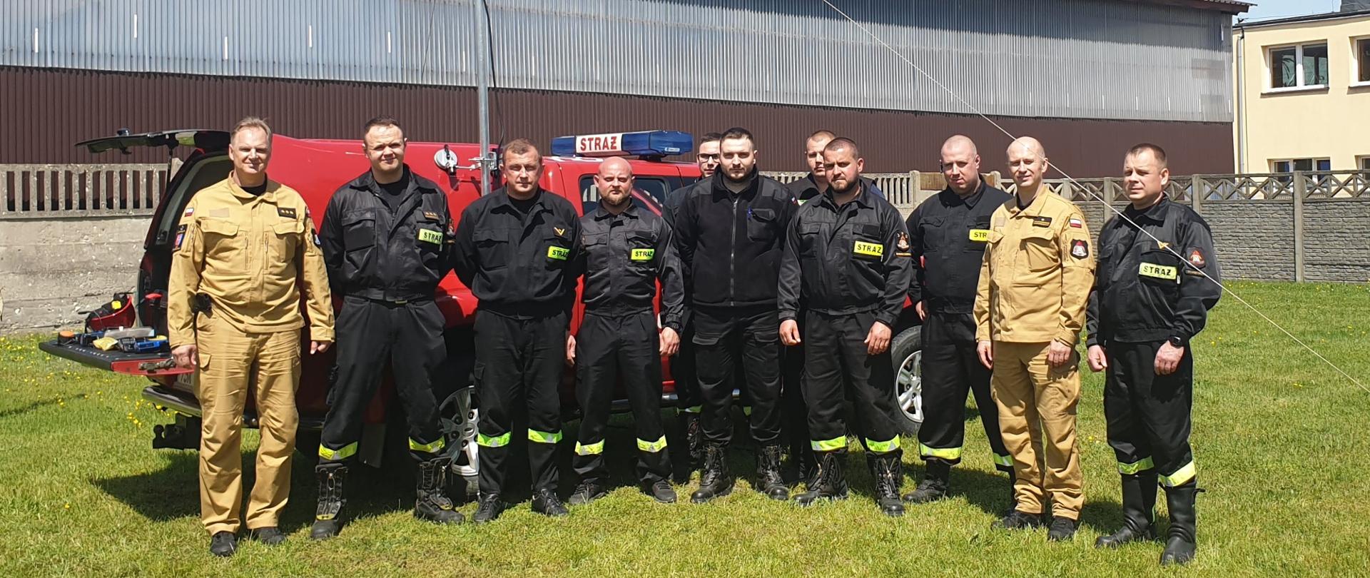 Grupowe zdjęcie osób, które ukończyły szkolenie wraz z osobami egzaminującymi na tle samochodu z JRG Skarżysko-Kamienna.