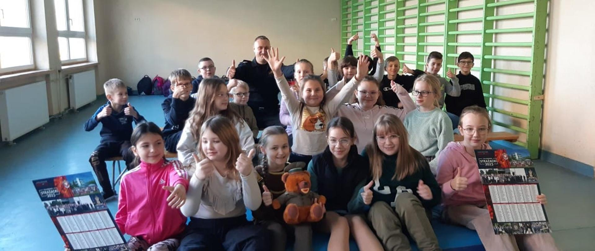 Na zdjęciu znajdują się uczniowie oraz strażak, sytuacja ma miejsce na sali 