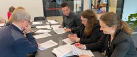 Grupa uczestników warsztatów siedząca przy stole analizująca materiały szkoleniowe.