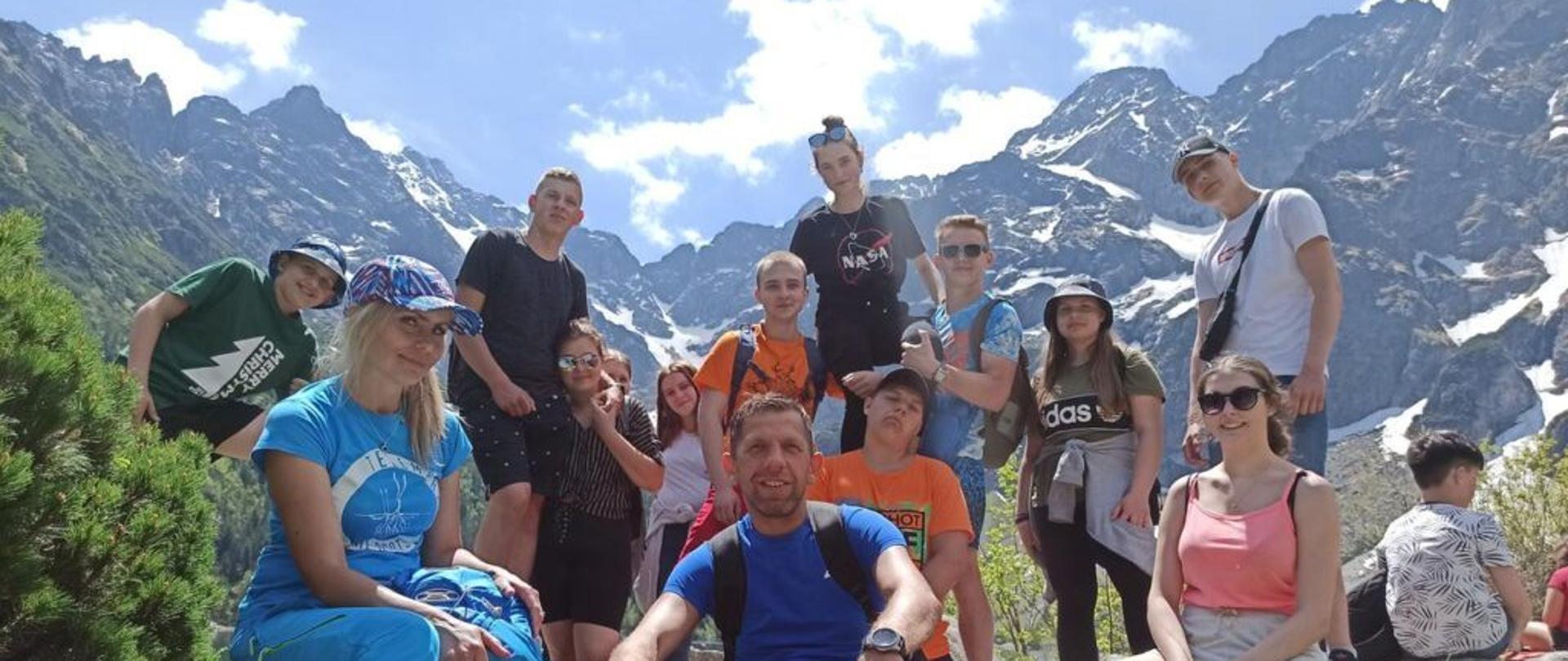 Grupa uczniów na wycieczce w górach. Ucznowie pozują do zdjęcia w pogodny dzień.