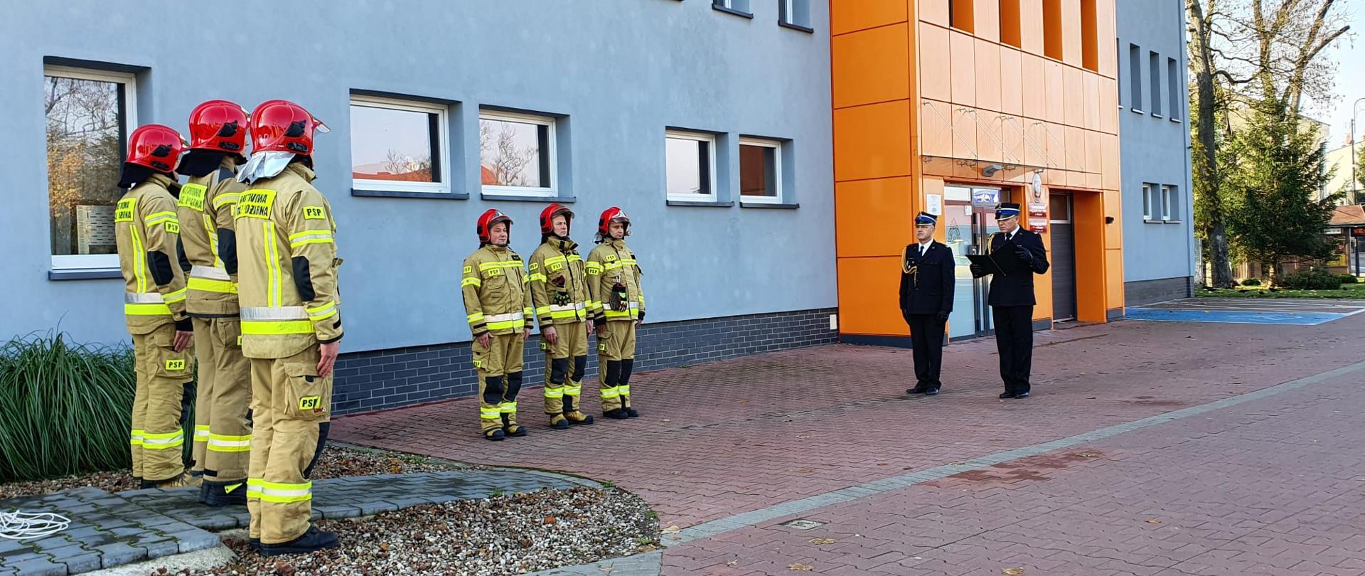 STRAŻACY W DWÓCH SZEREGACH, FUNKCJONARIUSZ ODCZYTUJE LIST