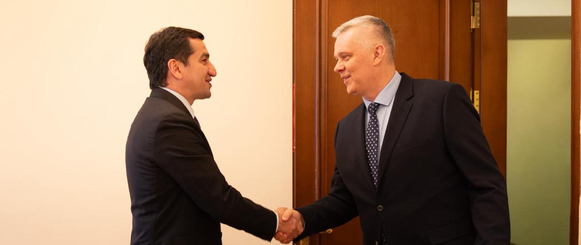 The photo shows the President’s foreign policy advisor, Hikmet Hajiyev (on the left), and Minister Tomasz Siemoniak (on the right) greeting each other. In the background, on the right, there is an open brown door. On the left, part of a chair is visible.